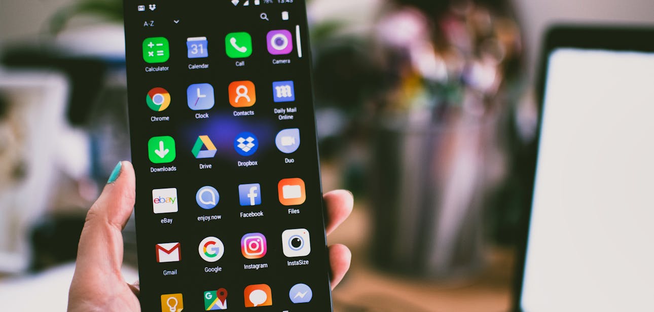 A close-up image of a person's hand holding a smartphone displaying various popular apps.