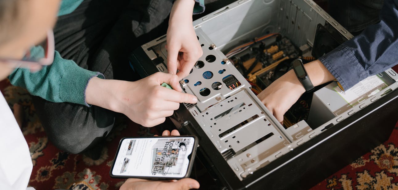 A close-up of hands fixing a computer with guidance from a mobile device.