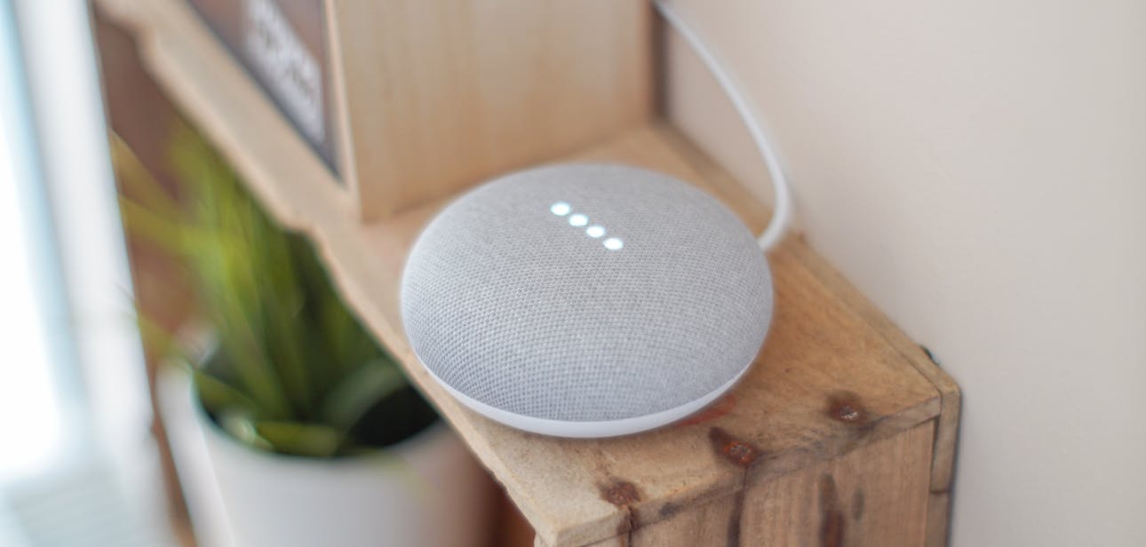 A Google Home Mini smart speaker on a wooden shelf, blending technology with home decor.
