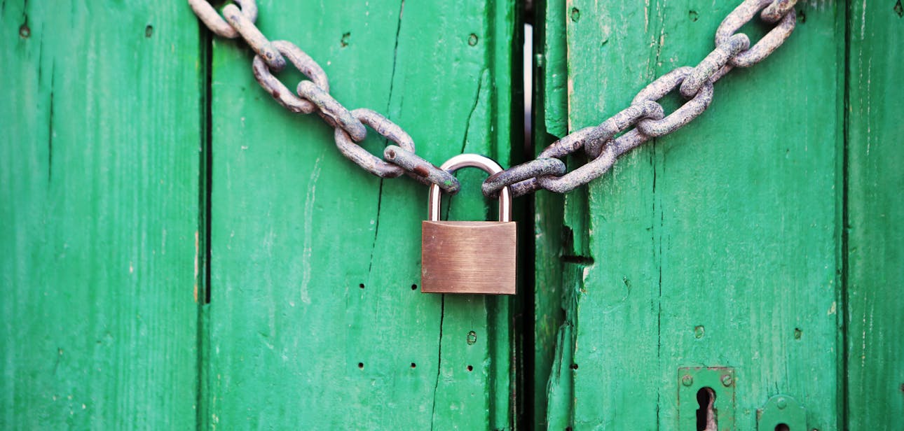 A rustic green wooden door secured with a heavy chain and padlock, symbolizing security.
