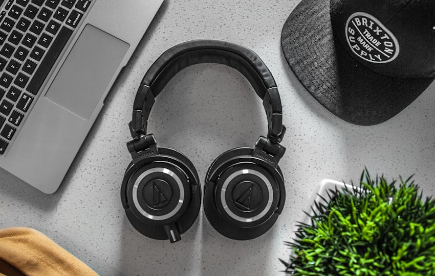 A stylish overhead shot of headphones with a laptop, cap, and decor on a desk.