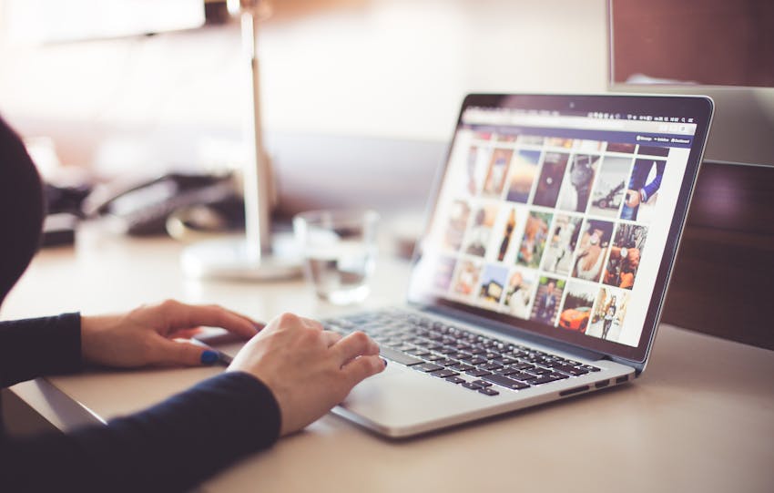 Close-up of hands typing on a laptop with an image gallery open on the screen.