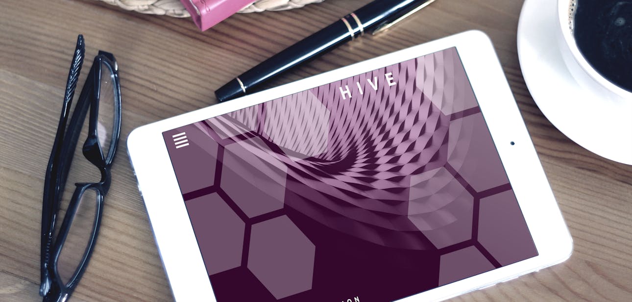 Flat lay of a modern workspace featuring a tablet displaying a screen, glasses, coffee, and a pen on a wooden desk.