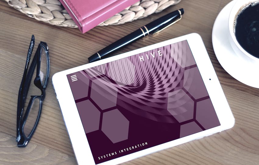 Flat lay of a modern workspace featuring a tablet displaying a screen, glasses, coffee, and a pen on a wooden desk.