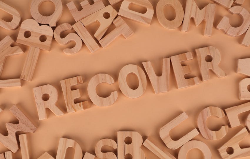 Flat lay of wooden alphabet letters with 'recover' highlighted.