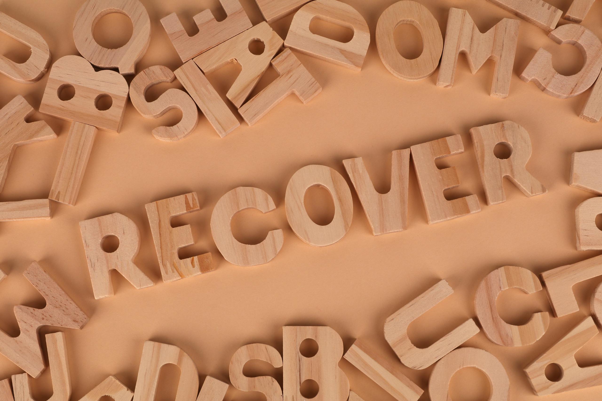 Flat lay of wooden alphabet letters with 'recover' highlighted.