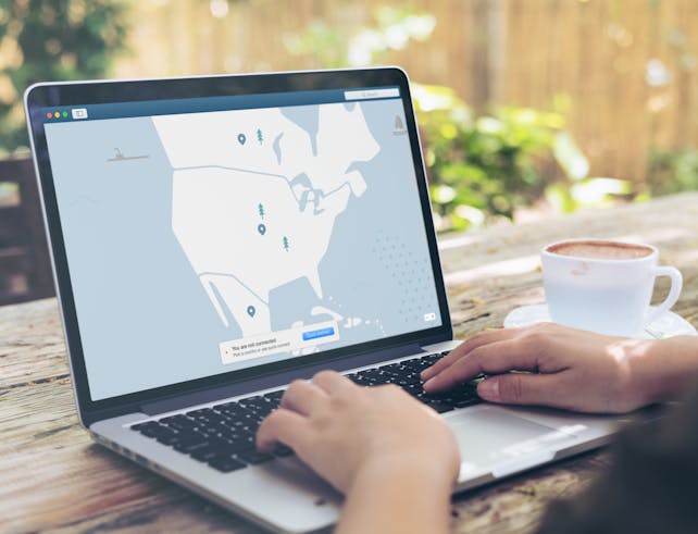 Hands typing on a laptop outdoors with a VPN interface displayed, next to a cup of coffee.