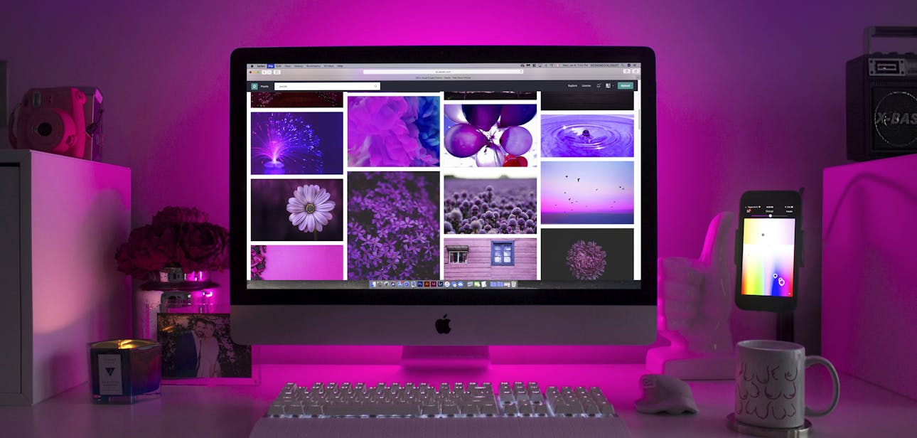 Modern desk setup with neon lighting and a desktop computer displaying colorful images.