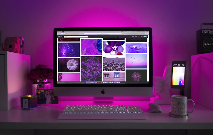 Modern desk setup with neon lighting and a desktop computer displaying colorful images.