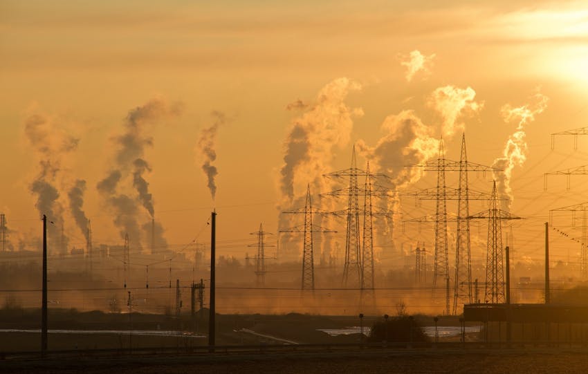 Silhouette of power lines and industrial smoke at sunset, highlighting pollution and energy themes.