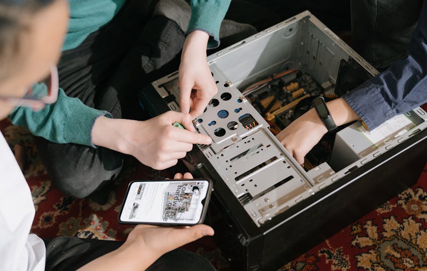 A close-up of hands fixing a computer with guidance from a mobile device.