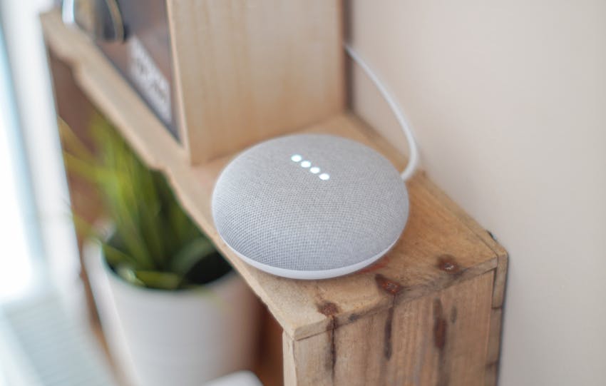 A Google Home Mini smart speaker on a wooden shelf, blending technology with home decor.