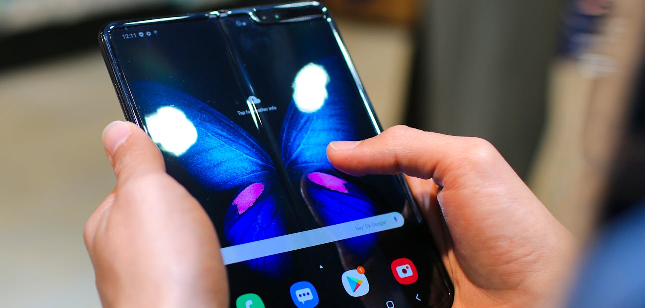 Close-up of hands holding a foldable smartphone showing a butterfly on the screen.