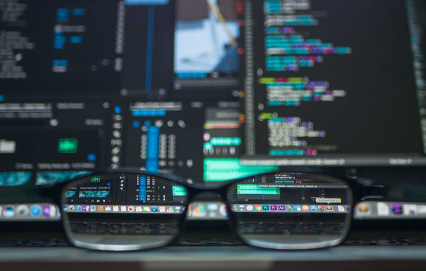 Eyeglasses reflecting computer code on a monitor, ideal for technology and programming themes.
