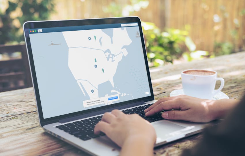Hands typing on a laptop outdoors with a VPN interface displayed, next to a cup of coffee.