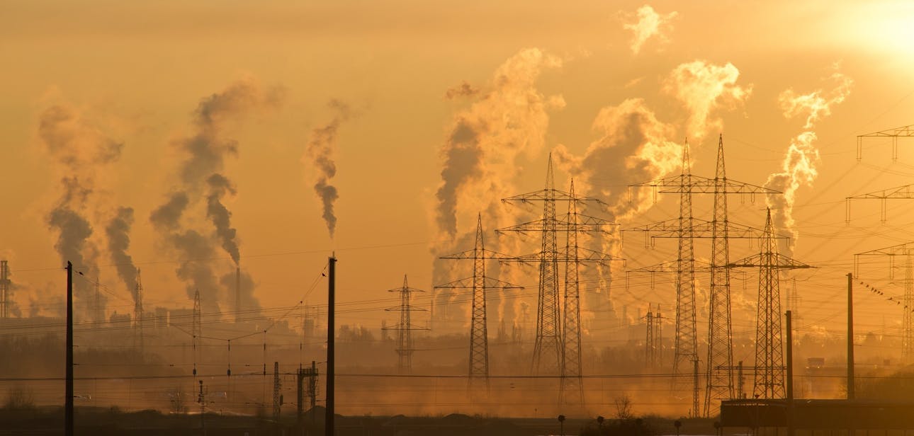 Silhouette of power lines and industrial smoke at sunset, highlighting pollution and energy themes.